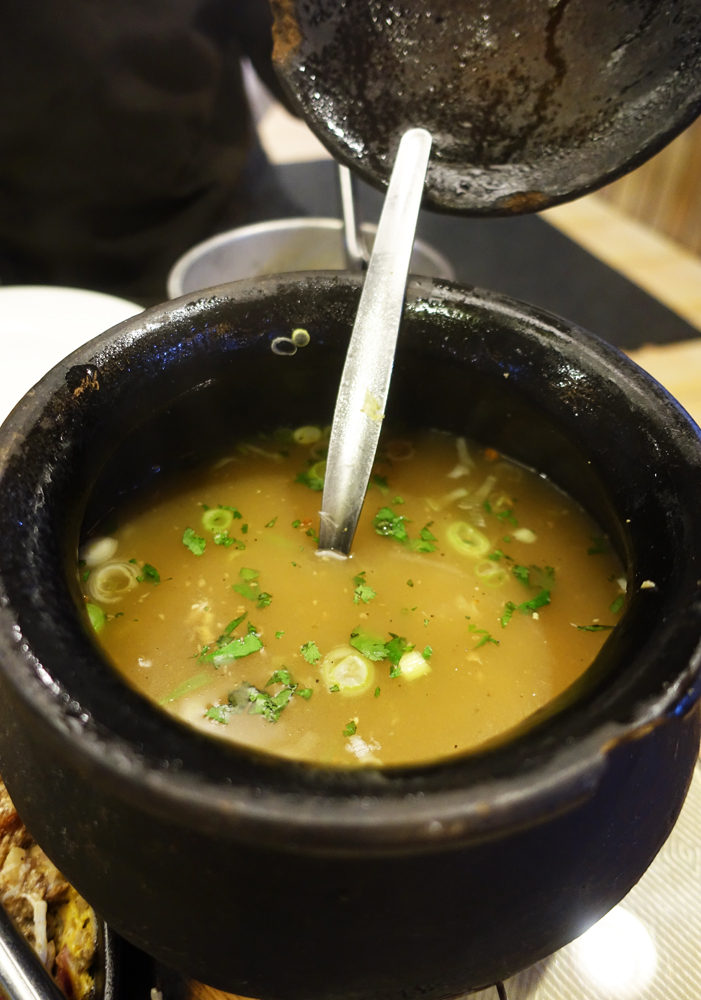 A photograph of soup in a black clay pot.