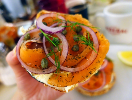 A close-up photo of bagel with lox; capers, dill, and onions on top of the salmon lox.